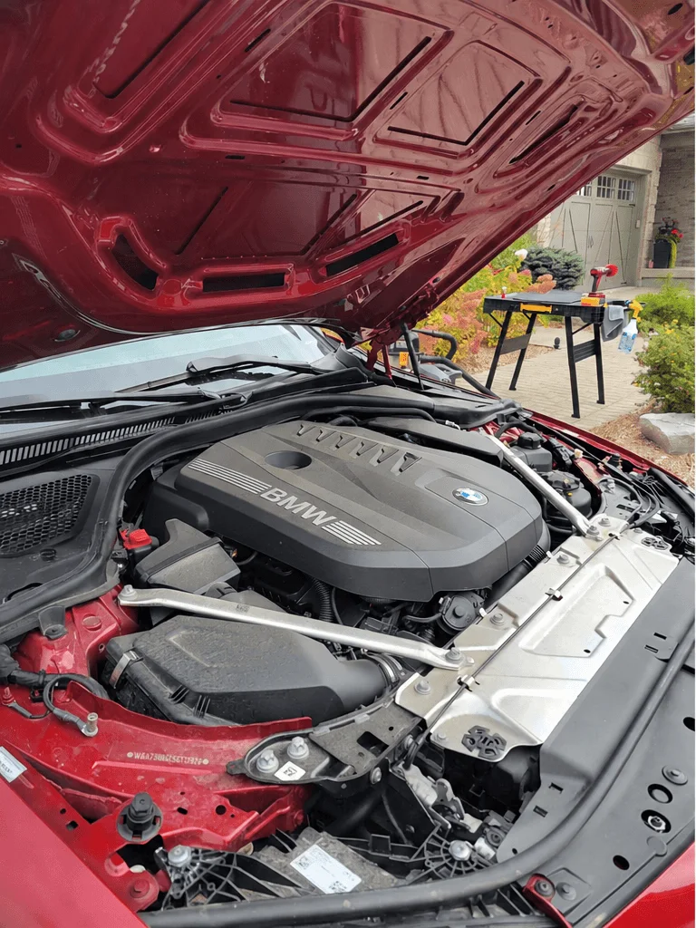 Before: engine bay of a red BMW M440i with dust on the covers and hood liner